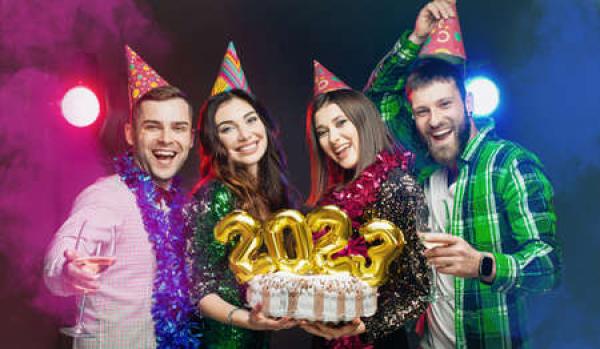 A group of friends with party hats holding a cake that has the numbers 2023 on it 